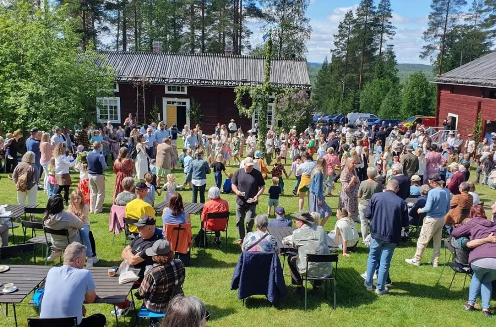 Traditional Midsummer celebration on a lawn with a maypole, sunshine, and lots of people.