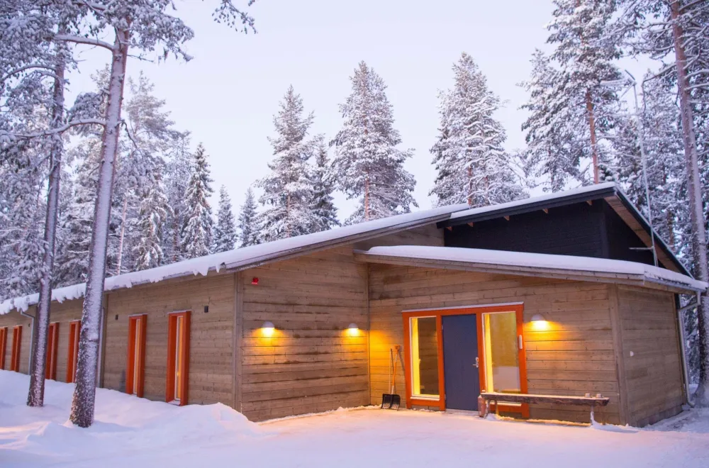 träbyggnad med röda fönsterfoder i en skog vintertid